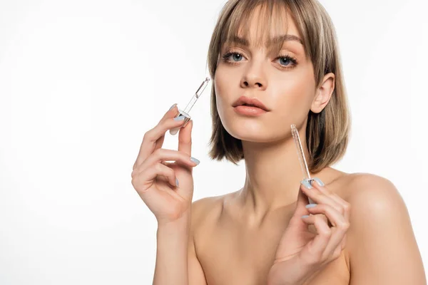 Young woman with bangs applying serum with pipettes isolated on white — стоковое фото