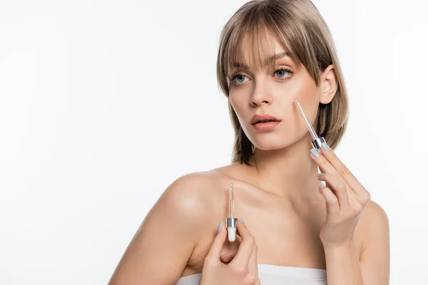 Mujer joven con flequillo sosteniendo pipetas y aplicando suero aislado sobre blanco - foto de stock