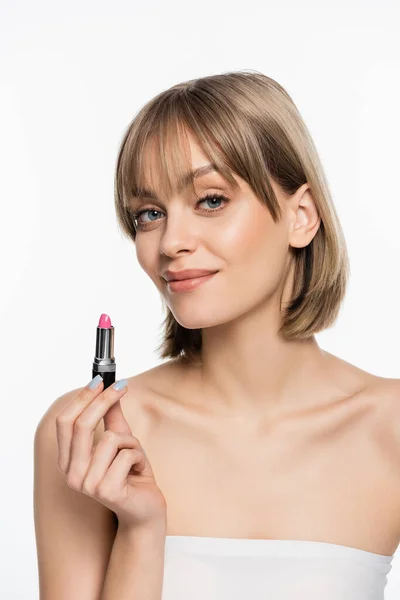Cheerful young woman with bangs holding pink lipstick isolated on white - foto de stock