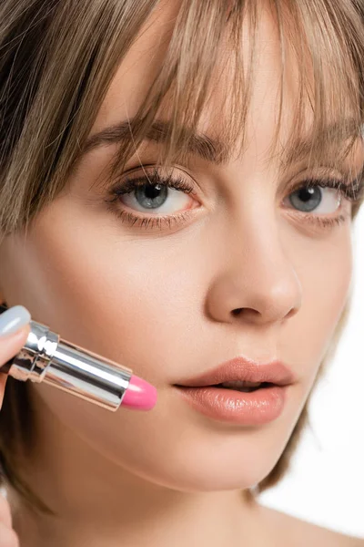 Close up view of young woman with bangs holding pink lipstick isolated on white — стоковое фото