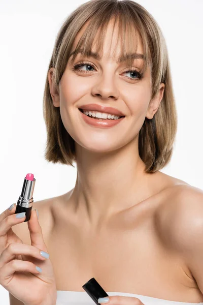 Joyful young woman with bare shoulders holding pink lipstick isolated on white — Stock Photo