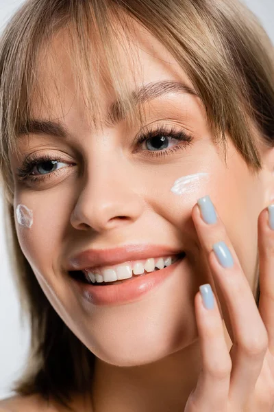Gros plan de femme heureuse avec frange appliquer de la crème sur les joues isolées sur blanc — Photo de stock