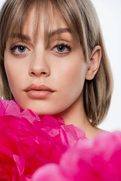 Mujer joven con flequillo y ojos azules cerca flor decorativa rosa aislado en blanco - foto de stock