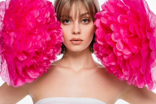 Blonde jeune femme regardant caméra près de fleurs rose vif isolé sur blanc — Photo de stock