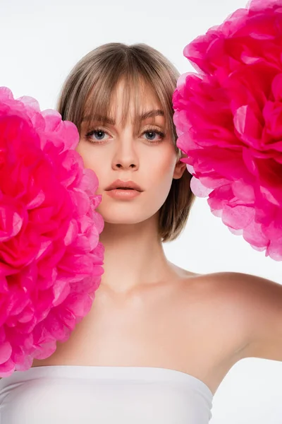 Blonde jeune femme avec épaule nue regardant caméra près de fleurs rose vif isolé sur blanc — Photo de stock