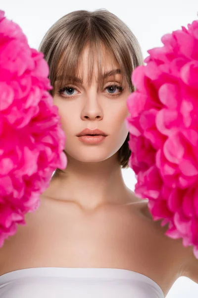 Молода жінка з блакитними очима дивиться на камеру через розмиті рожеві квіти ізольовані на білому — стокове фото