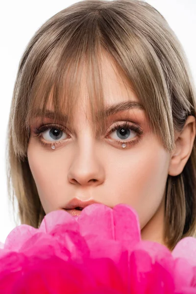 Young woman with bangs and shiny rhinestones under blue eyes near pink flower isolated on white — Fotografia de Stock