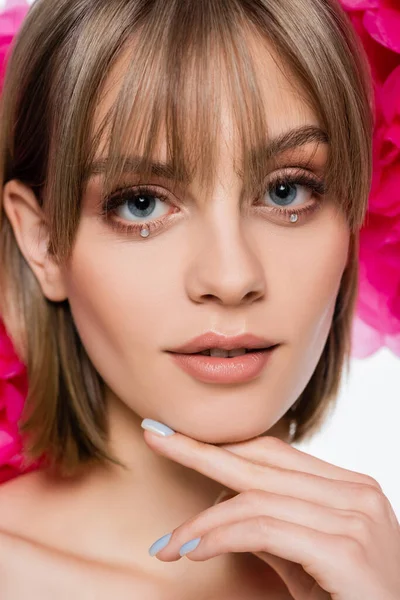 Young woman with bangs and rhinestones under blue eyes near pink flowers isolated on white — Foto stock