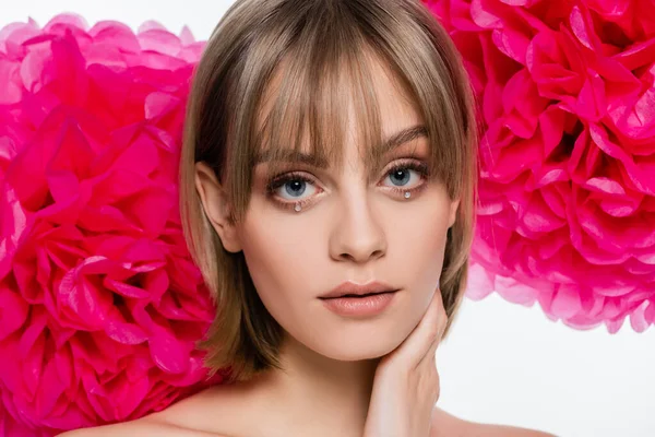 Pretty young woman with bangs and rhinestones under blue eyes near pink flowers isolated on white — Photo de stock