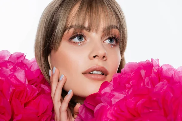 Jovem mulher com strass sob olhos azuis olhando para longe perto de flores rosa isolado no branco — Fotografia de Stock