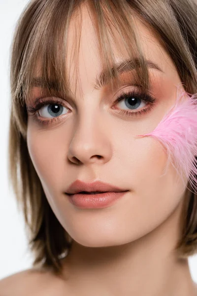 Close up view of young woman with blue eyes and pink feather on face isolated on white - foto de stock