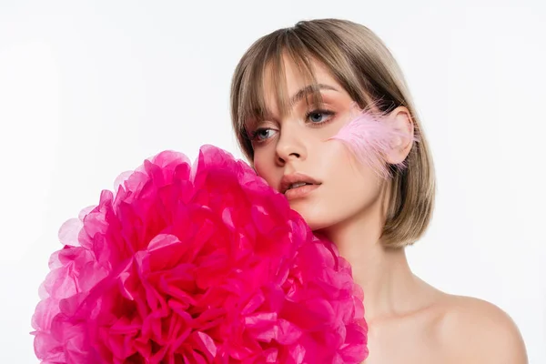 Junge Frau mit Feder auf der Wange in der Nähe leuchtend rosa dekorative Blume isoliert auf weiß — Stockfoto