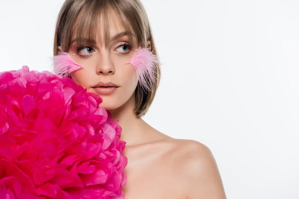 Jolie femme avec des éléments décoratifs en maquillage et plumes roses sur les joues près de fleur lumineuse isolé sur blanc — Photo de stock