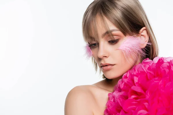 Mujer joven con elementos decorativos en maquillaje y plumas en las mejillas cerca de flor aislada en blanco - foto de stock