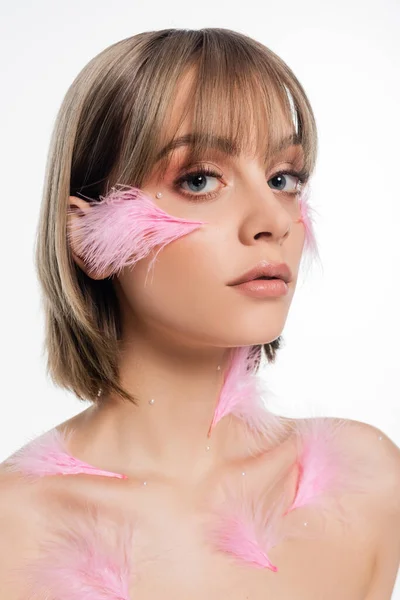 Mujer joven con elementos decorativos en la cara y el cuerpo y plumas de color rosa en las mejillas aisladas en blanco - foto de stock