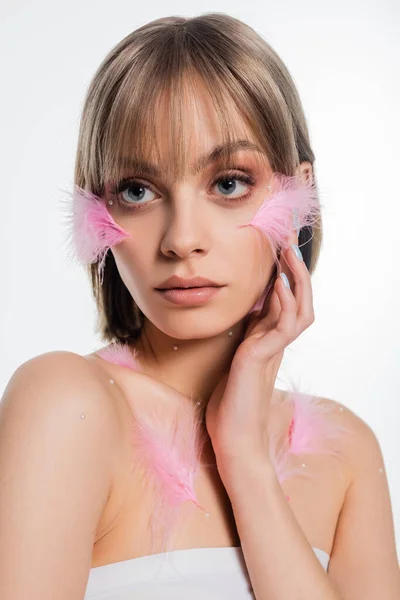 Bonita mujer joven con elementos decorativos en la cara y el cuerpo y plumas de color rosa en las mejillas aisladas en blanco - foto de stock