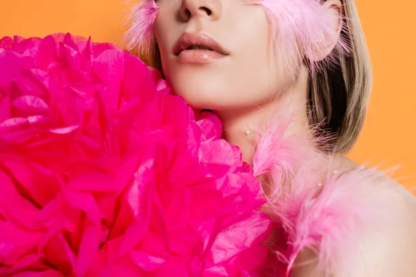 Cropped view of woman with decorative beads and feathers on body near pink flower isolated on orange — стоковое фото