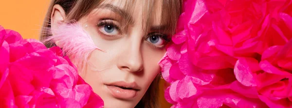 Woman with feather on cheek near pink flowers isolated on orange, banner — Foto stock