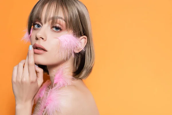 Young woman with decorative beads in makeup and pink feathers on body isolated on orange - foto de stock