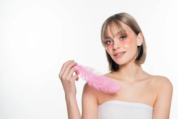 Heureuse jeune femme avec des patchs hydrogel oeil tenant plume rose isolé sur blanc — Photo de stock