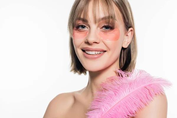 Jeune femme souriante avec des patchs hydrogel oeil tenant plume rose isolé sur blanc — Photo de stock