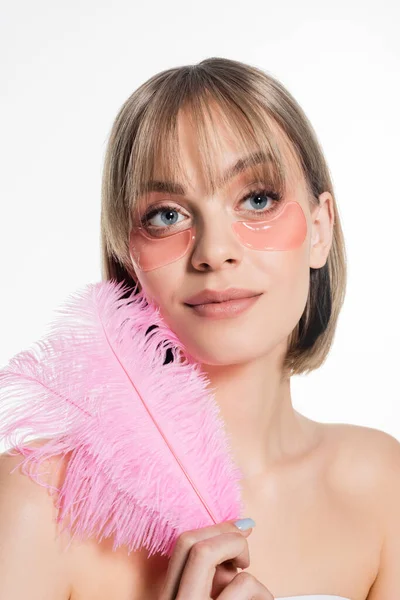 Pleased young woman with hydrogel eye patches holding pink feather isolated on white - foto de stock
