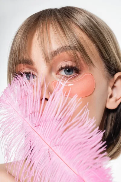 Young woman with hydrogel eye patches covering face with soft pink feather isolated on white — Foto stock