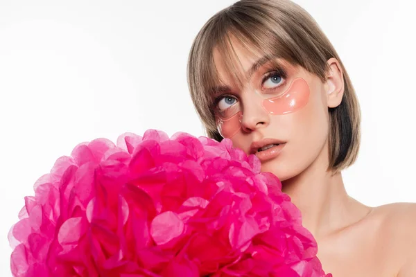 Junge Frau mit Hydrogel-Augenklappen, die in der Nähe einer leuchtend rosa Blume wegschauen, isoliert auf weißem Grund — Stockfoto