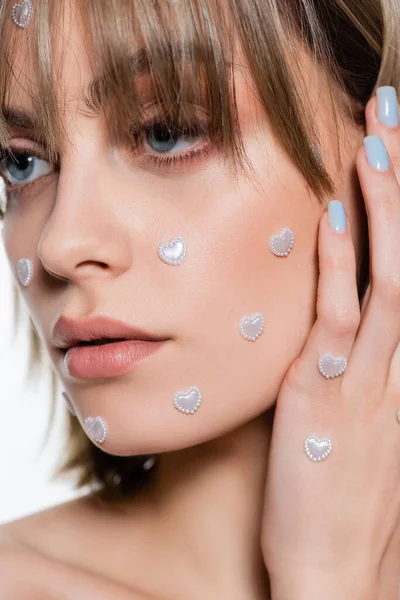 Vista de cerca de la mujer bonita con elementos creativos de la forma del corazón en el maquillaje aislado en blanco - foto de stock