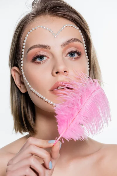 Pretty woman with creative heart shape beads on face holding pink feather isolated on white - foto de stock