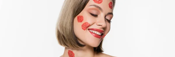 Pleased young woman with red kiss prints on cheeks and body smiling isolated on white, banner - foto de stock