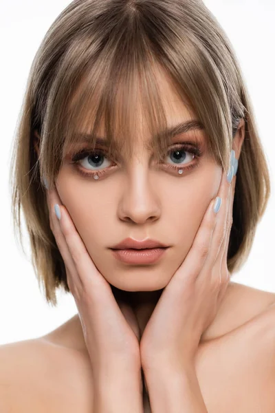 Jolie jeune femme aux épaules nues et aux strass brillants sous les yeux bleus touchant le visage isolé sur blanc — Photo de stock