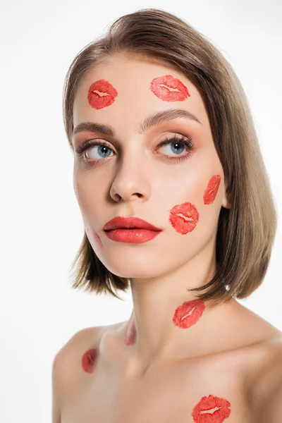 Mujer joven con huellas de beso rojo en la cara mirando hacia otro lado aislado en blanco - foto de stock