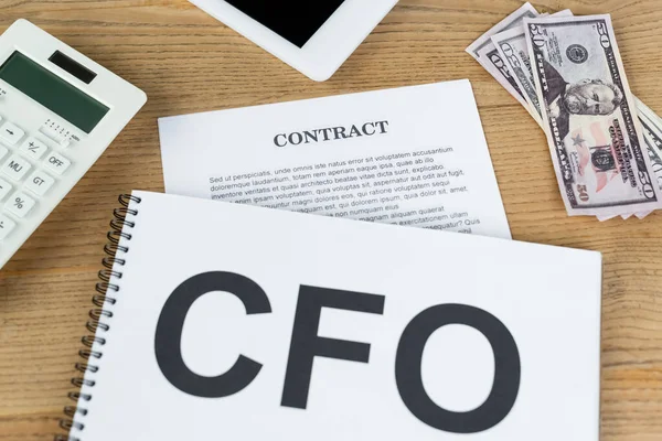 Draufsicht auf Papiere mit CFO und Vertragsaufdruck in Dollarnähe, digitales Tablet und Taschenrechner auf dem Schreibtisch — Stockfoto