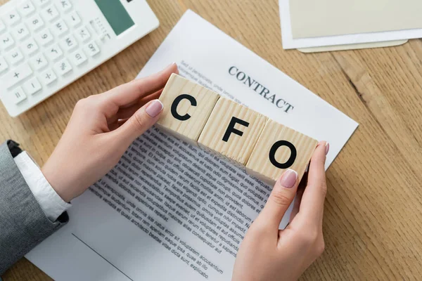 Vista dall'alto donna d'affari in possesso di cubi di legno con cfo lettering vicino contratto e calcolatrice — Foto stock