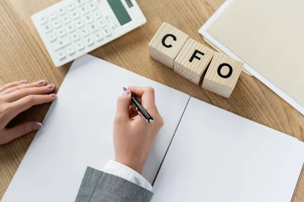 Top view of businesswoman writing near calculator and cubes with cfo lettering on desk — Stock Photo