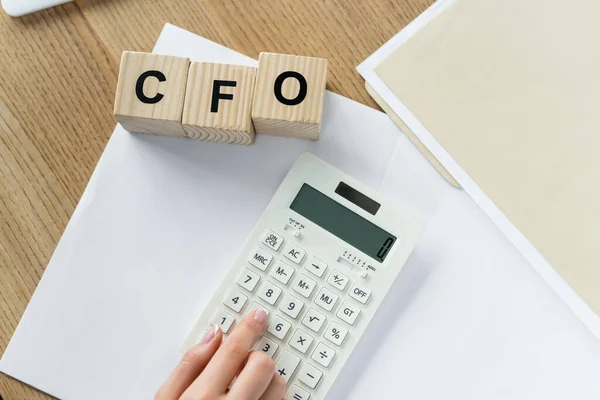 Top view of chief financial officer using calculator near cubes with cfo lettering — Stock Photo