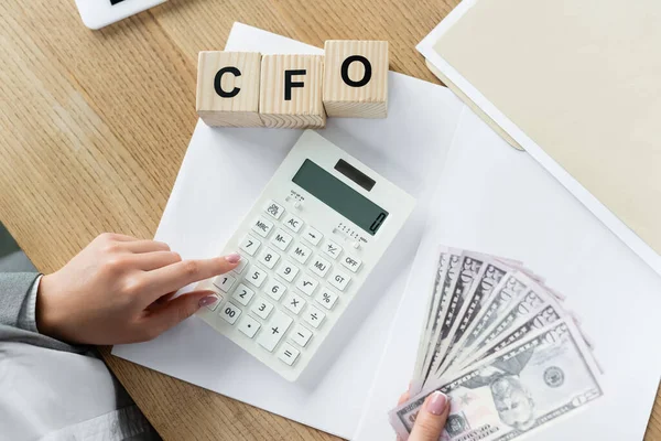 Vista dall'alto di Chief Financial Officer utilizzando calcolatrice e tenendo dollari vicino cubi con cfo lettering — Foto stock