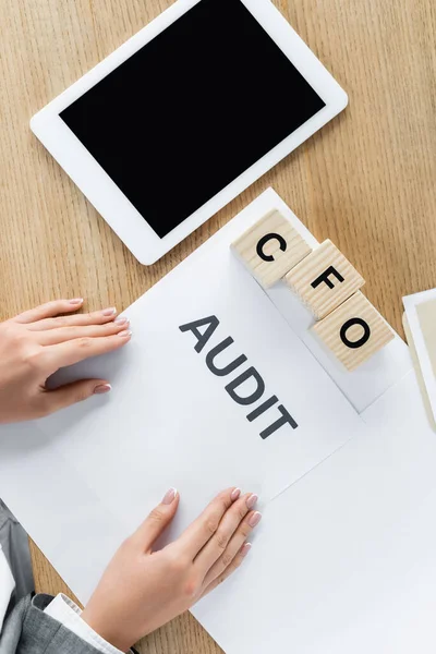 Vista superior de mujer de negocios cerca de documento con letras de auditoría, cubos con cfo y tableta digital con pantalla en blanco - foto de stock