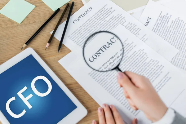 Cropped view of woman holding magnifier near contract and digital tablet with cfo lettering — Stock Photo