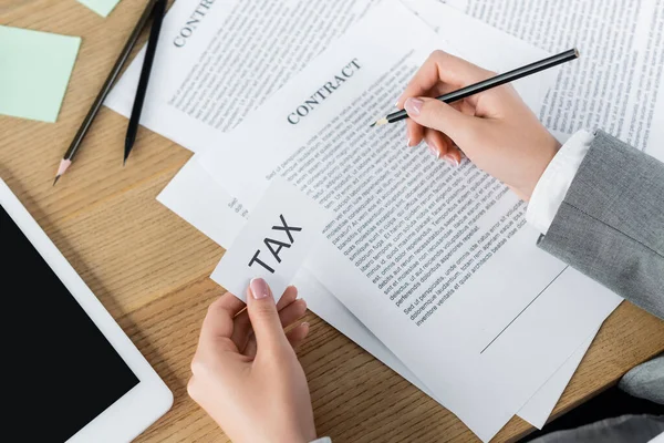 Обрезанный вид налогового инспектора, держащего бумагу с налоговой надписью при проверке контракта возле цифрового планшета — стоковое фото