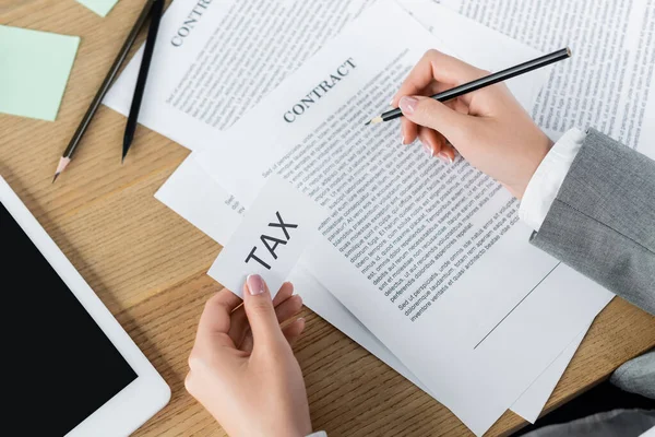 Ausgeschnittene Ansicht des Steuerinspektors, der Papier mit Steueraufdruck hält, während er den Vertrag in der Nähe des digitalen Tablets überprüft — Stockfoto