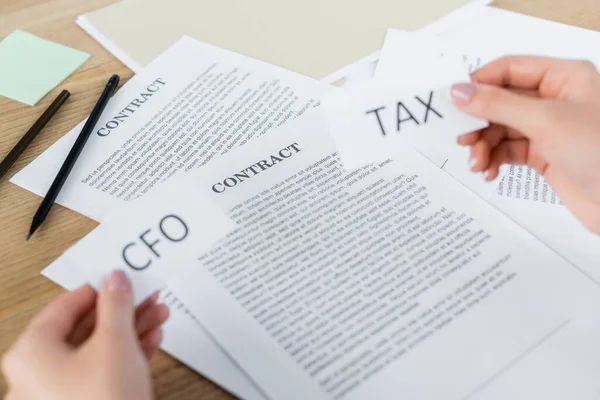 Cropped view of woman holding papers with tax and cfo lettering near contract on desk — Stock Photo