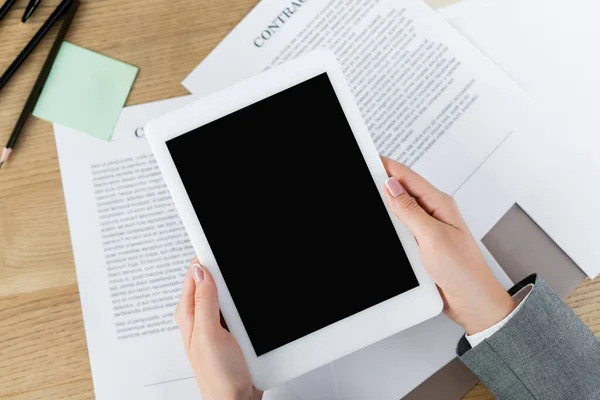 Обрезанный вид женщины, держащей цифровой планшет с чистым экраном над бумагами с контрактом — стоковое фото