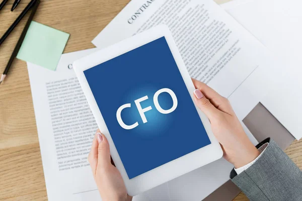 Cropped view of woman holding digital tablet with cfo lettering on screen above papers with contract — Stock Photo