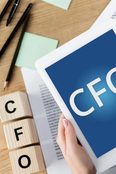 Cropped view of businesswoman holding digital tablet with cfo letters on screen near wooden cubes — Stock Photo