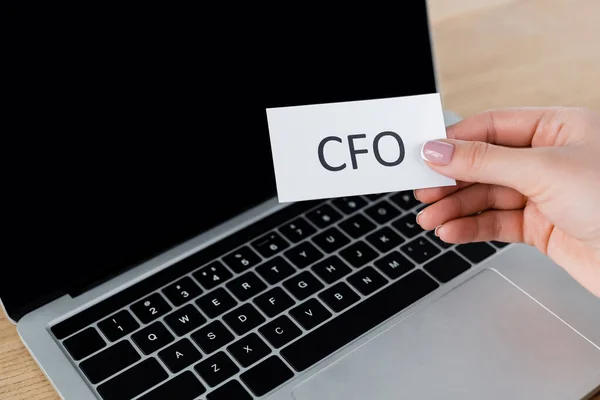 Cropped view of businesswoman holding paper with cfo lettering near laptop — Stock Photo