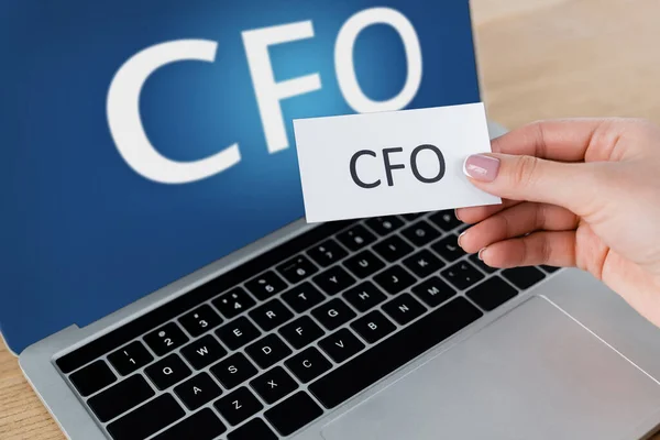 Cropped view of woman holding paper near laptop with cfo lettering on screen — Stock Photo