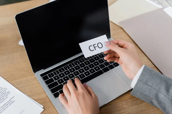 Ausgeschnittene Ansicht einer Frau, die Papier mit cfo-Schriftzug hält und Laptop benutzt — Stockfoto