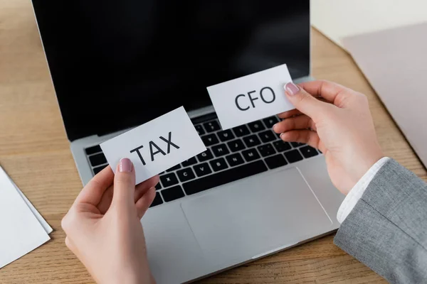 Cropped view of tax inspector holding papers with tax and cfo lettering near laptop — Stock Photo